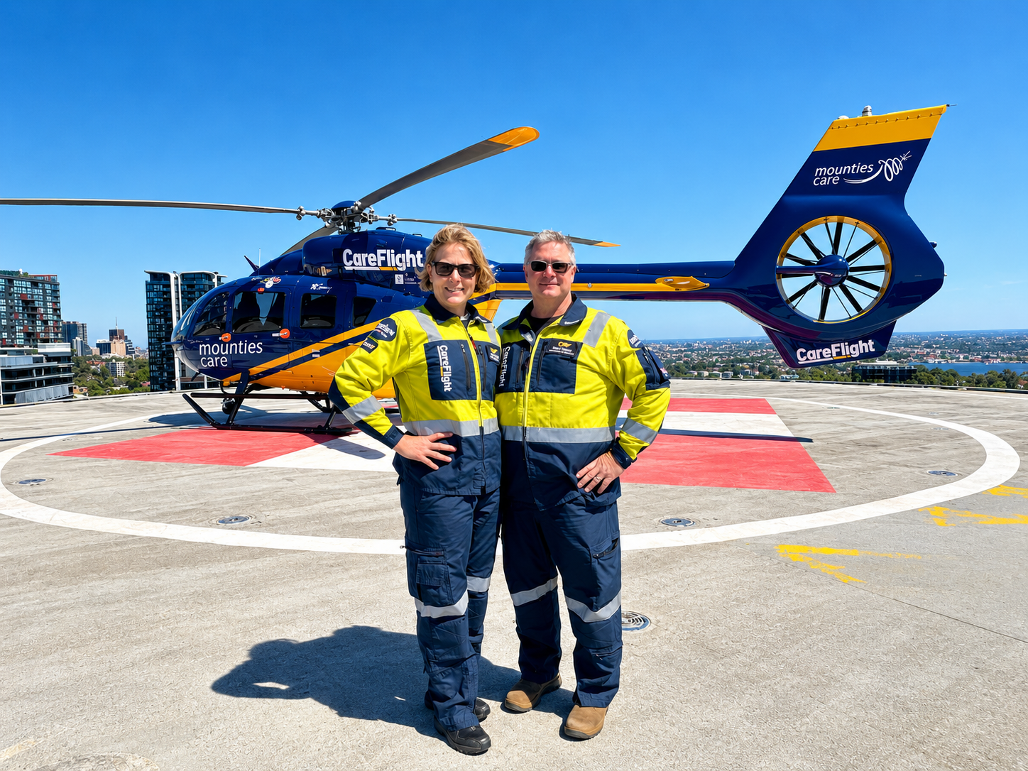 Dr Ruth and Brian Parsell in high-visibility uniforms in front of a CareFlight helicopter on a helipad